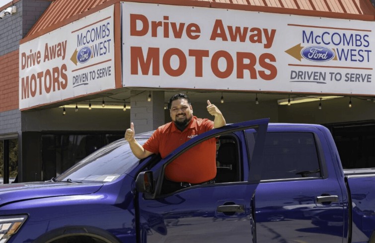Un vendedor de Red McCombs Drive Away Motors West sonríe junto a una camioneta frente a la tienda en Culebra Road en San Antonio